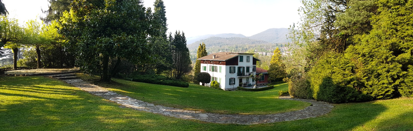 Vista panoramica del giardino e della villa tra gli alberi, con le montagne sullo sfondo